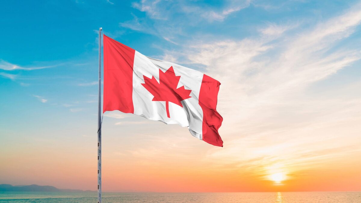 Sun setting behind the ocean with a Canadian flag waving in the foreground.